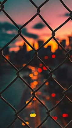 the city lights are seen through a chain link fence