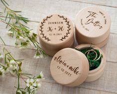 three personalized wooden boxes with wedding rings in them on a table next to flowers