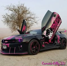 a black car with pink and white designs on it's doors is parked in the desert