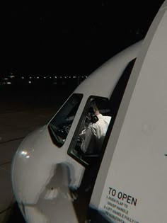 a man sitting in the cockpit of an airplane at night with his feet out the window