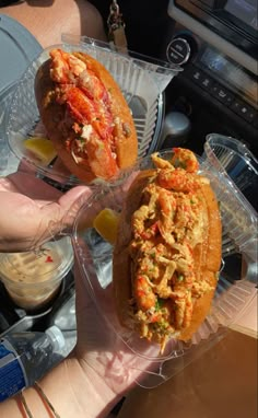 two sandwiches in plastic containers sitting on top of a car dash board next to a person's hand