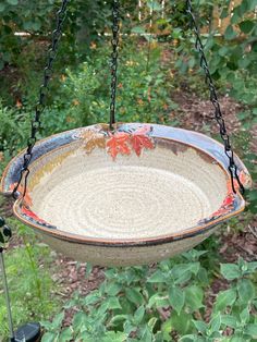 a bird feeder hanging from a chain in the grass with leaves painted on it's side