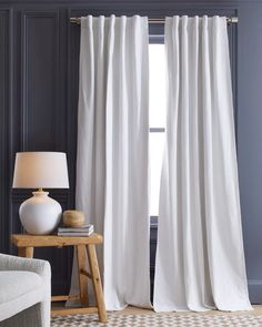 a living room with white drapes and a lamp on the side table in front of it