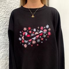 a woman wearing a black nike sweatshirt with flowers and stars on the front, standing in front of a white wall