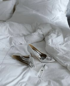 two pairs of white high heeled shoes laying on a bed with sheets and pillows