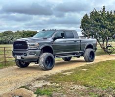 a large gray truck parked on top of a dirt road next to a wooden fence