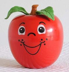 an apple with a face drawn on it sitting on a white tableclothed surface