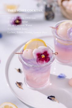 two glasses filled with drinks on top of a white plate next to lemon slices and flowers