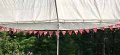 a large white tent with red and white flags hanging from it's sides in front of trees