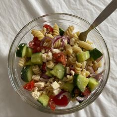 a glass bowl filled with pasta salad on top of a white table cloth next to a fork