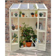 an outdoor greenhouse with potted plants and pots on the side walk in front of a brick wall