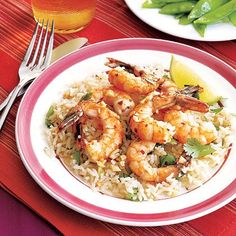 shrimp and rice with lime wedges on a red place mat next to a glass of orange juice