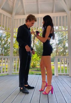 a man in a suit standing next to a woman wearing high heels and holding a rose