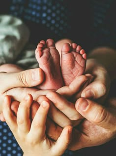 two hands holding a baby's feet while laying on top of another persons hand