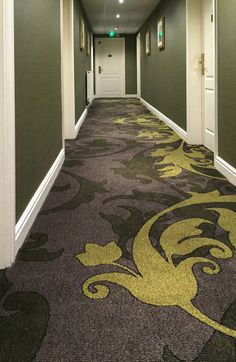 a long hallway with green and yellow carpeting on both sides, leading to another room