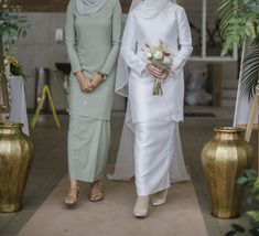 two women standing next to each other in front of vases with flowers on them