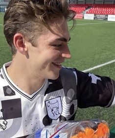 a young man sitting on top of a soccer field holding a bag of carrots