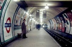 a man standing in the middle of a subway station next to a train track with advertisements on it