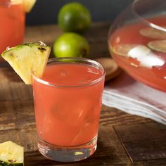 two glasses filled with watermelon and pineapple drink next to limes on a cutting board