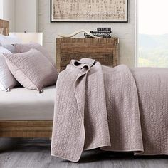 a bed with a blanket and pillows on top of it next to a wooden dresser