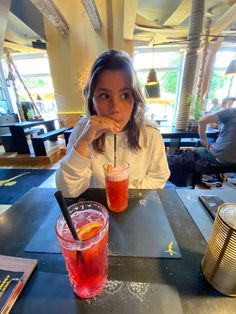 a woman sitting at a table with two drinks in front of her