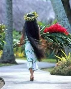 a woman walking down a sidewalk with flowers on her head and long hair in the wind