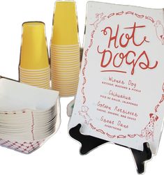 there are many plates and cups on the table with a sign that says hot dogs