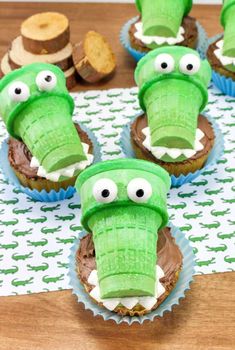 cupcakes with green icing and fake alligator heads on them sitting on a table