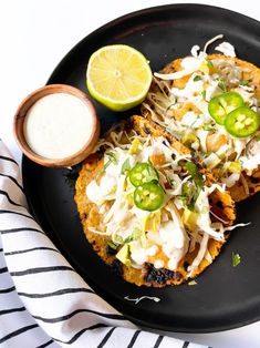 two tacos on a black plate with limes and sour cream