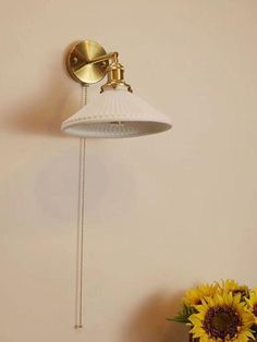 a white lamp on the wall next to a vase with sunflowers