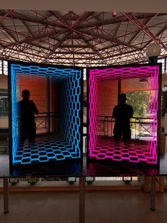 two people standing in an open area with neon colored squares on the walls and floor