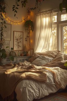 an unmade bed sitting next to a window in a room with plants hanging from the ceiling