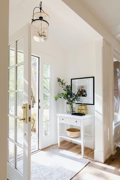 an entryway with a white table, mirror and plant on the door way to another room