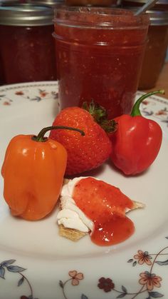 three tomatoes and two peppers sitting on a plate next to some jam in a jar