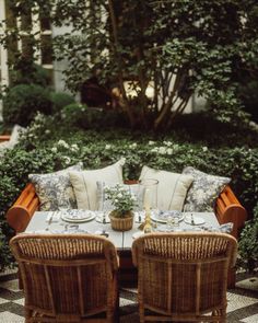 an outdoor dining area with wicker chairs and table set for four, surrounded by greenery