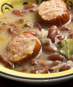 a yellow and white bowl filled with beans, meat and broth next to a green leaf