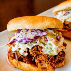 two pulled pork sandwiches with coleslaw and slaw on a white platter