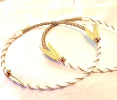 two bracelets with gold leaves on them sitting on a white cloth covered tablecloth