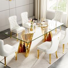 a glass dining table with white chairs and gold trimmings on the legs, in front of a window