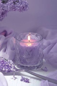 a lit candle sitting on top of a table next to purple flowers and a spoon