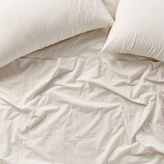 an unmade bed with white sheets and pillows