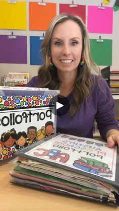 a woman sitting at a desk holding up a stack of children's books in front of her