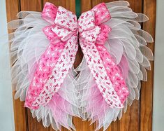 a pink and white wreath hanging on the front door with ribbon around it's bow