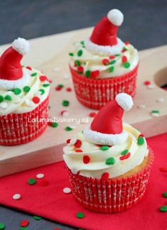 three cupcakes with white frosting and santa hats on top, sitting on a red napkin