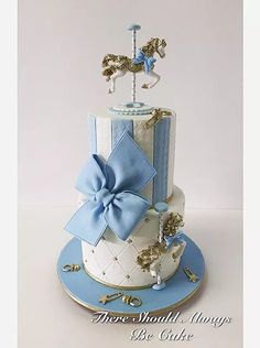 a three tiered cake decorated with blue and white ribbon, gold decorations and a horse on top