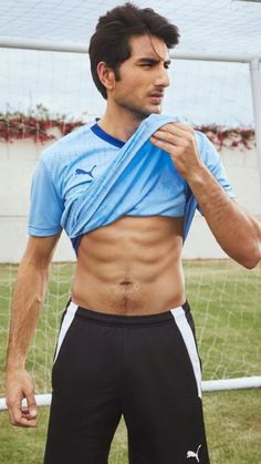 a shirtless man standing in front of a soccer goal wearing black and white shorts