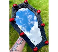 a person's hand holding up a mirror with cherries on it and the sky in the background