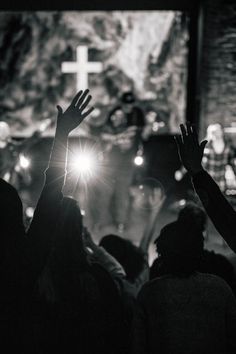 people raising their hands in front of a cross