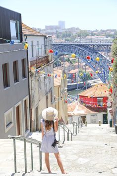 a woman in a white dress and hat is standing on some stairs looking at the bridge