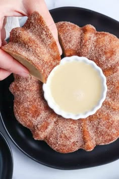 someone is dipping something into a small bowl on a black plate with powdered sugar